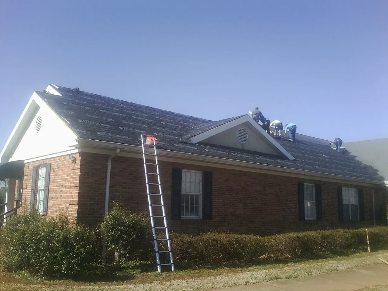 Crew tearing shingles off a brick ranch roof with a ladder set — Emergency Roof Repair work by our crew in Eureka