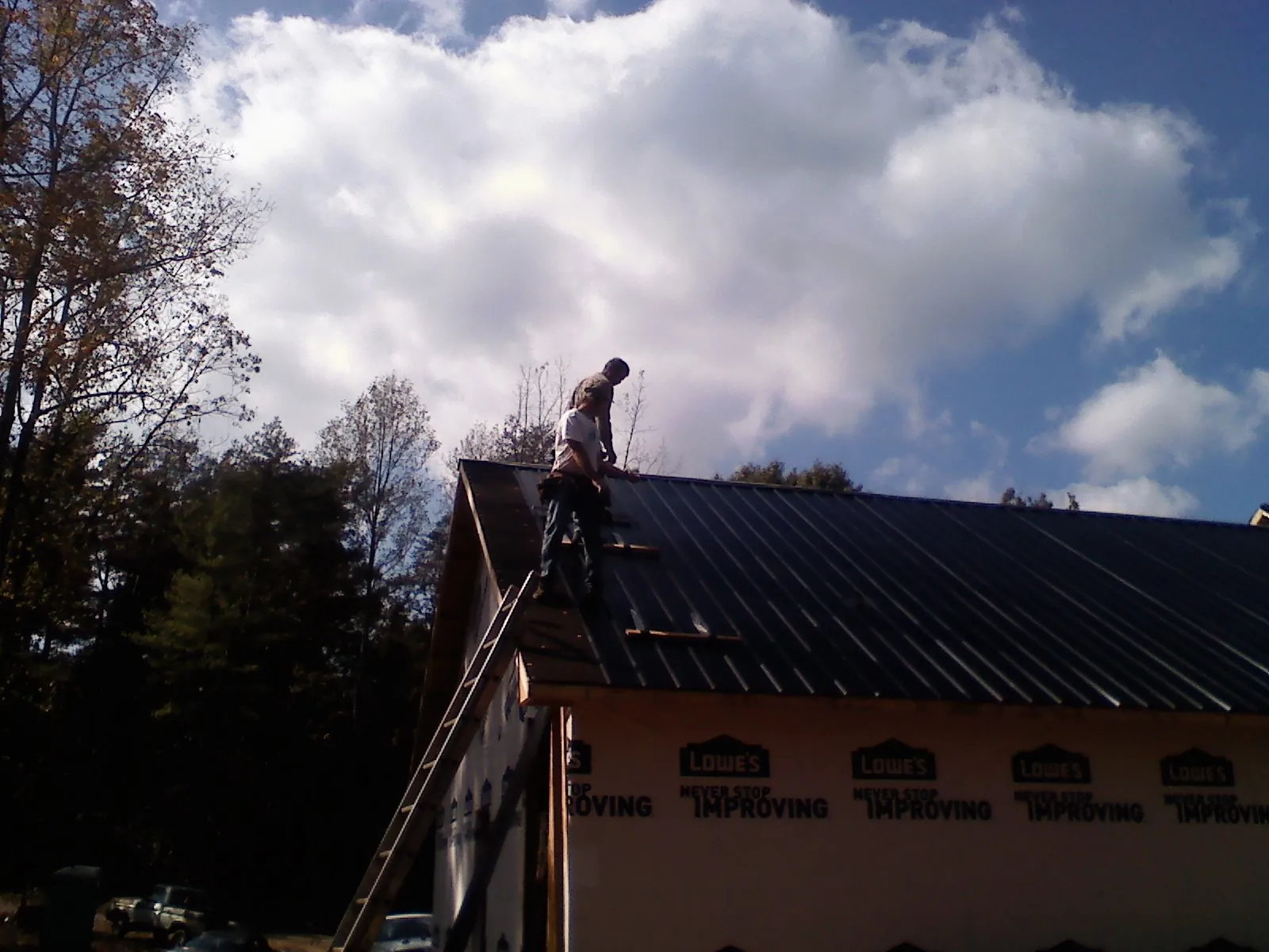 Roofer fastening dark metal panels high against a cloudy sky, from a Roof Inspection job in Eureka
