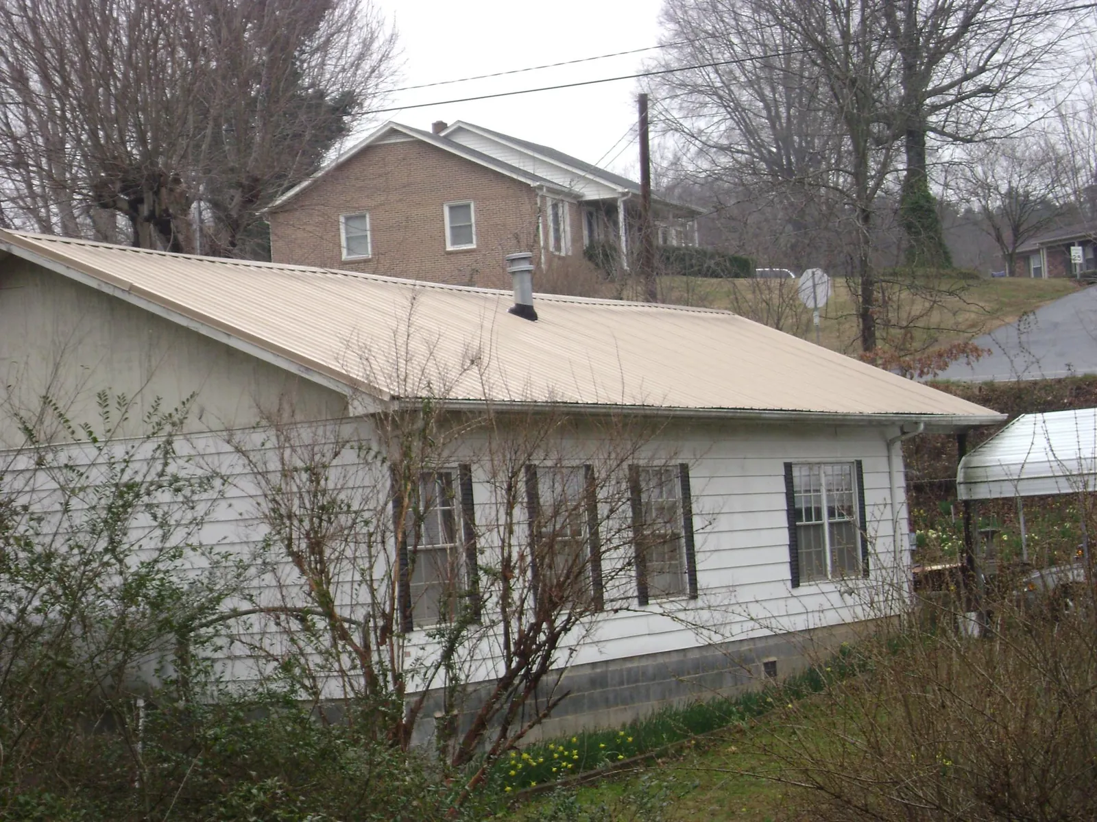 Tan metal roof on a white sided house set into a hillside — Commercial Roofing by Roofing Brothers in Eureka
